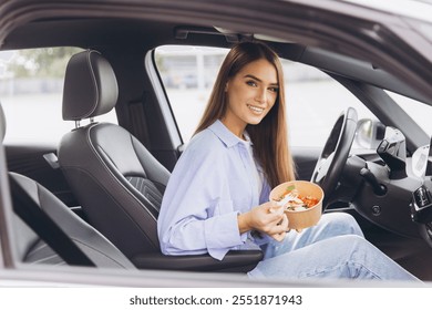 A young woman sits in her car eating a healthy salad, capturing the essence of a quick and nutritious meal during a busy day. - Powered by Shutterstock