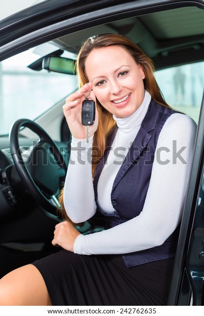 Young woman sits in new car on driver seat\
in a car dealership, obviously she is buying the auto, or she has\
bought the car and holding the keys in\
hand