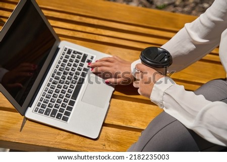Young woman sits on bench with a laptop and coffee
