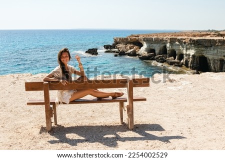 Young woman sits on a bench near sea cliffs at Cape Greco viewpoint, enjoying the scenery and natural beauty.