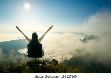 Young woman sits on a chair and open her arms at the top of the mountain, Success in business concept