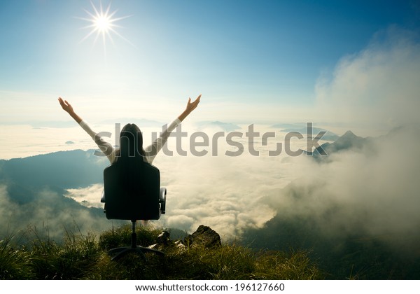 Young woman sits on a chair\
and open her arms at the top of the mountain, Success in business\
concept