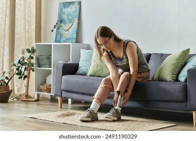 A young woman sits on a couch in her living room, adjusting the prosthetic leg she is wearing. - Powered by Shutterstock