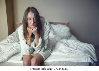 A Young Woman Sits On The Edge Of The Bed Closing Her Eyes And Propping Her Head In Her Hands. Fatigue, Depression, Insomnia, Quarantine, Isolation