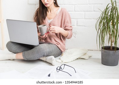 Young Woman Sits On The Floor In A Scandinavian Apartment Interior With A Laptop, Studying Law, Freelance Girl At Work, Distance Learning Student, Online Employment, Paperwork And Outsourcing Concept