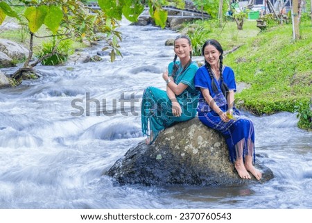 A young woman sits on a rock with water flowing over it. Sit on a rock stream Brook, Stream ,Mountain river Creek Flowing Over Rock in Rainforest Fresh natural water. women dressed in a Karen costume