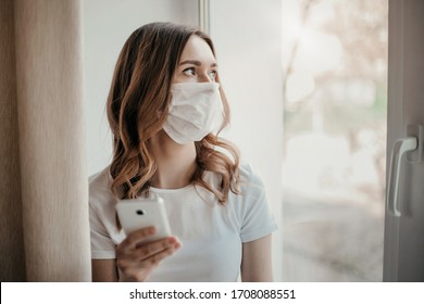 Young Woman Sits On A Windowsill And Looks Out The Window, Holds A Mobile Phone In Her Hands, Quarantine Coronavirus, Job Search, Depression, Isolation