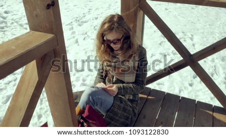 A young woman sits on a wooden veranda, silently touching the origami paper plane with her fingers and putting it on her knees. Girl sitting outdoors with white aerogamy aircraft, close view, 4k