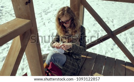 A young woman sits on a wooden veranda, silently touching the origami paper plane with her fingers and putting it on her knees. Girl sitting outdoors with white aerogamy aircraft, close view, 4k