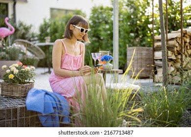 Young Woman Sits With Phone At Backyard Of Her Countryhouse, Spending Summer Time At Cozy Garden