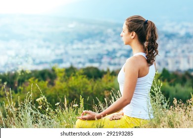 Young woman sits in yoga pose with city on background. Freedom concept. Calmness and relax, woman happiness.