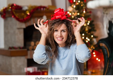 Young Woman Sitting Alone, In Front Of Christmas Tree ,holding A Gift Ribbon Over Her Head.