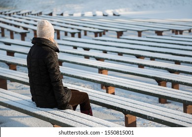 Young woman sitting alone on wooden bench in sunny winter day. Snow covered bleachers. Thinking about life. Back side view. - Powered by Shutterstock