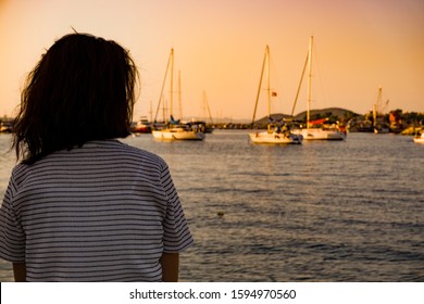 Young Woman Sitting Alone On Seaport Coast At Sunset, Looking At Distant Seascape Horizon. Say Good Bye. Miss Someone. Desire, Hope / Time To Go Far Away. Girl Feel Lonely At Beautiful Blue Seaside.