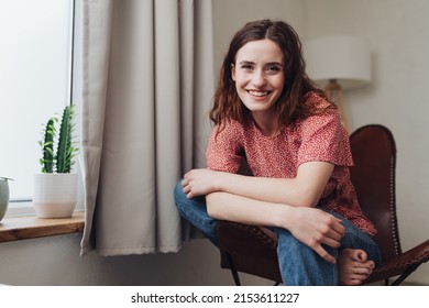 Young Woman Sitting Barefoot In Leather Chair Looking At Camera