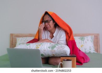 A young woman sitting in bed watching film on her laptop, crying. A cup of tea and a box of tissue paper in front of her. - Shutterstock ID 2196802253
