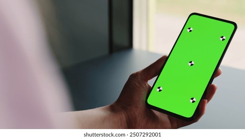 young woman sitting at the black table near window and holding smartphone with vertical green screen - Powered by Shutterstock