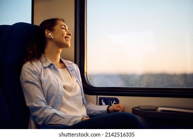 Young woman sitting by the window in a train and enjoying in music with eyes closed during her journey. Copy space.