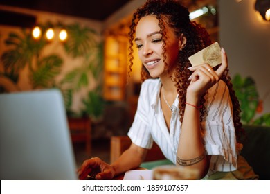 Young Woman Sitting At Cafe Making Online Shopping, Using Credit Card And Laptop. Online Shopping, E-commerce, Internet Banking, Spending Money. Black Friday.