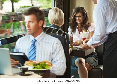 Young woman sitting in cafe, waiter serving sweets. Businessman eating club sandwich and working in the forground. Selective focus on women. - Powered by Shutterstock