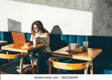 Young Woman Sitting At Caffe, Drinking Coffee And Working On Laptop.