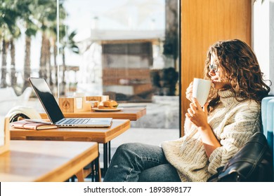 Young Woman Sitting At Caffe, Drinking Coffee And Working On Laptop.