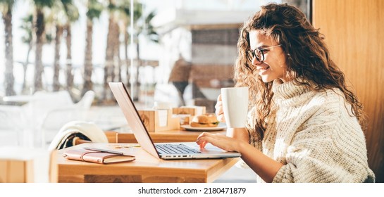 Young Woman Sitting At Caffe, Drinking Coffee And Working On Laptop.