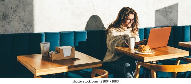 Young woman sitting at caffe, drinking coffee and working on laptop.