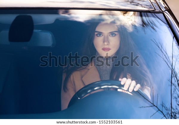 a young woman\
sitting in a car behind the wheel.she\'s going to go. in the glass\
of the car reflection of the\
sky.