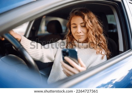 Young woman sitting in a car in the driver's seat looking into a smartphone, paying for parking and navigating in the city Foto stock © 