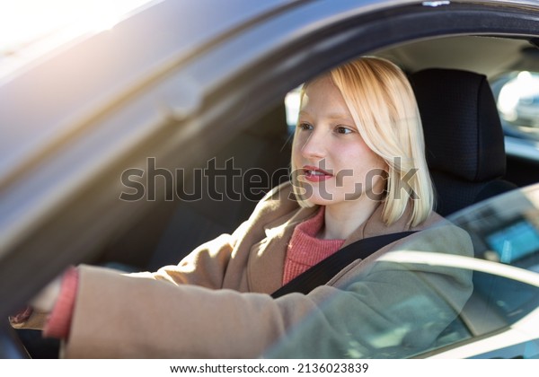 Young woman sitting in a\
car. Happy woman driving a car and smiling. Portrait of happy\
female driver steering car with safety belt. Cute young lady happy\
driving car.