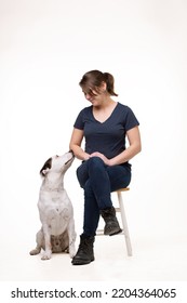 Young Woman Sitting In A Chair Looking Down At Her Pit Bull Or Pitbull Terrier Dog With Amusement As He Is Looking Up At Her With A Loving Expression