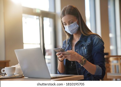 Young Woman Sitting At Coffee Shop And Working On Laptop With Face Mask