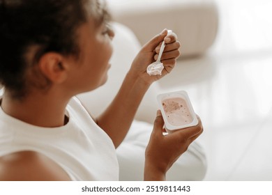 Young woman is sitting comfortably and savoring a spoonful of strawberry yogurt - Powered by Shutterstock