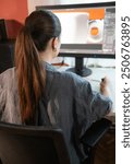 A young woman is sitting at a computer in the office, doing graphic design