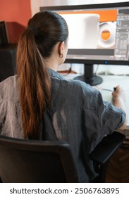 A young woman is sitting at a computer in the office, doing graphic design