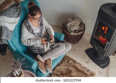 Young woman sitting in a cozy armchair, with a warm blanket, using a mobile phone - Shutterstock ID 1831527934