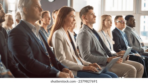 Young Woman Sitting in a Crowded Audience at a Business Conference. Female Attendee Writing Important Information on a Laptop. Keynote Speech in an Auditorium with Successful Businesspeople. - Powered by Shutterstock