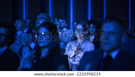 Young Woman Sitting in a Crowded Audience at a Business Conference. Female Attendee Cheering and Clapping After a Motivational Keynote Speech. Auditorium with Young Successful Businesspeople.