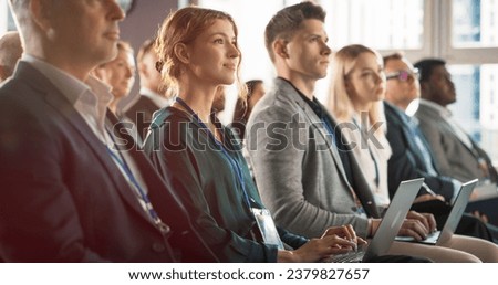 Young Woman Sitting in Crowded Audience at Business Conference. Female Delegate Smiling and Using Laptop Computer. Manager Watching Motivational Presentation About Investing In Innovative Startups.