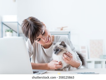 Young Woman Sitting At Desk And Cuddling Her Lovely Cat, Togetherness And Pets Concept