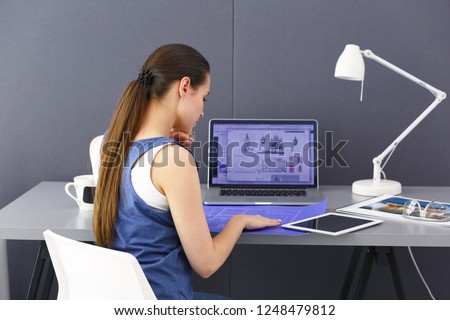 Young woman sitting at the desk with instruments, plan and laptop.
