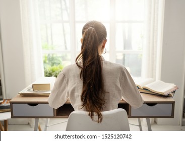 Young Woman Sitting At Desk And Studying At Home, She Is Reading Books, Back View