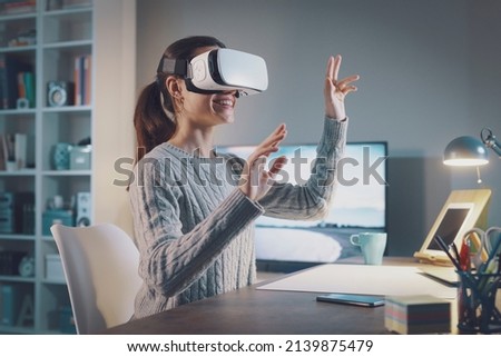 Young woman sitting at desk and wearing a VR headset, she is interacting with virtual reality