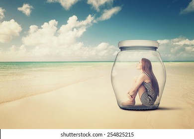 young woman sitting in a glass jar on a beach looking at the ocean view. Loneliness outlier person. After storm survivor message to future generation concept 