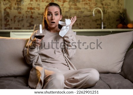 A young woman is sitting with a glass of red wine and watching TV. A young woman watches a sad movie in depression and cries. 