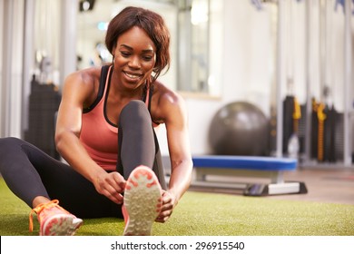 Young woman sitting in a gym tying her shoelaces, horizontal - Powered by Shutterstock