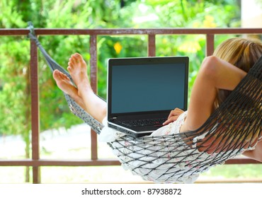 Young Woman Sitting In A Hammock In A Garden With Laptop