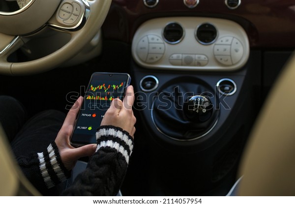 Young woman sitting in her car reviewing and\
investing in the stock market with technical indicator tools on his\
smartphone. Trading\
concept.