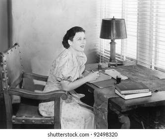 Young Woman Sitting At Her Desk Writing A Letter